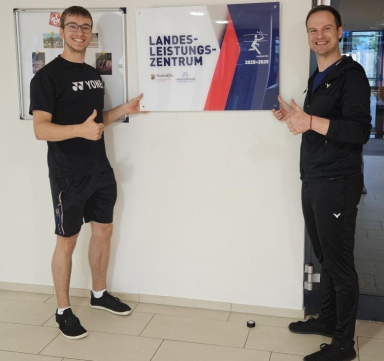 Zwei Personen vor einem Schild des Landesleistungszentrums Badminton, LLZ, LSB