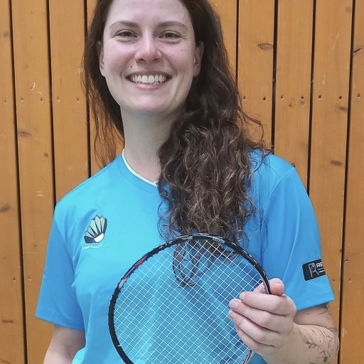 Bianca Hofert im blauen Trikot mit Badmintonschläger vor Holzpaneelen