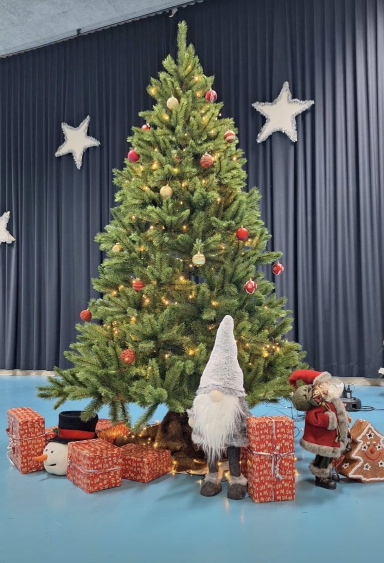 Weihnachtsbaum mit Geschenken, Weihnachtsmann-Figur und Weihnachtsdeko vor blauem Vorhang