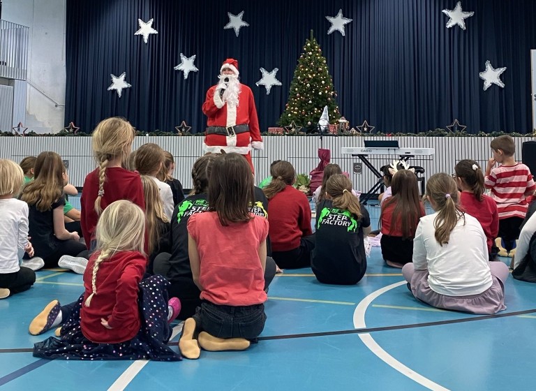 Weihnachtsfeier mit Weihnachtsmann, Kindern und geschmücktem Weihnachtsbaum in einer festlich dekorierten Halle