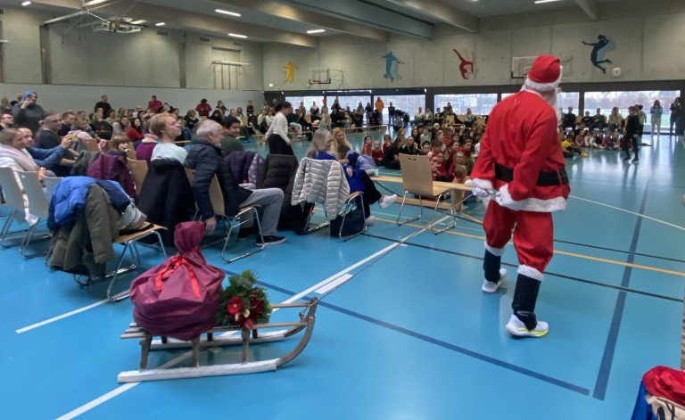 Weihnachtsfeier in einer Turnhalle mit Publikum, Weihnachtsmann und Schlitten