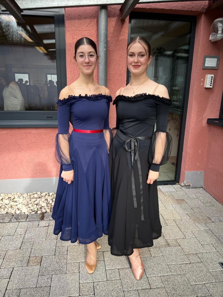 Zwei Frauen in eleganten Abendkleidern, blau und schwarz, vor einem Gebäude
