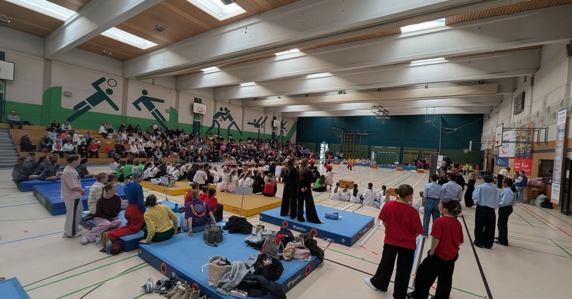 Turnwettkampf in einer Sporthalle mit vielen Zuschauern und jungen Teilnehmern auf Matten