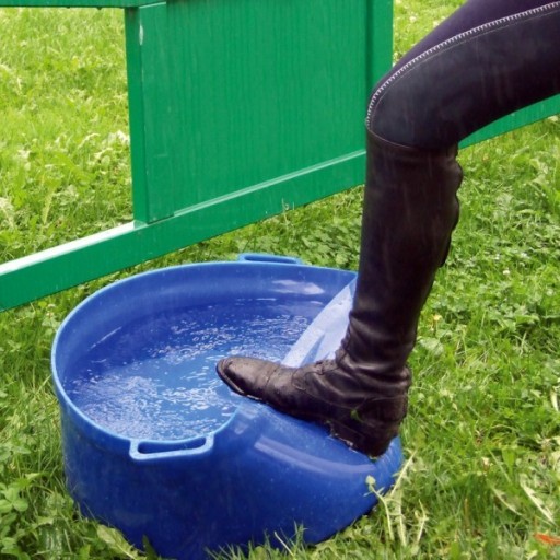 Reiterstiefel im blauen Wassertrog auf einer Wiese reinigen Reiterstiefel wird in einem blauen Kunststoff-Wassertrog auf einer Wiese gereinigt