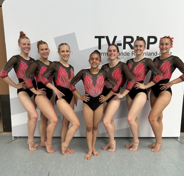 Turnmannschaft des Turnverbands Rheinland-Pfalz beim Wettkampf vor TV-RLP Banner Turnmannschaft des Turnverbands Rheinland-Pfalz in Gymnastikanzügen vor TV-RLP Banner