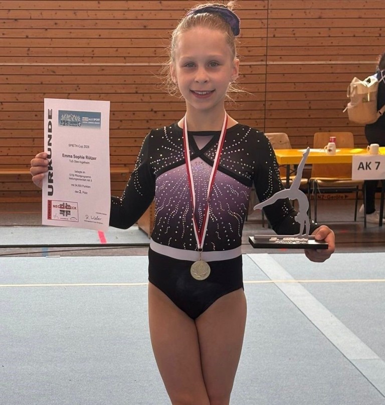 Emma R. gewinnt beim SPETH-Cup 2023 einen Turnwettbewerb und hält Urkunde sowie Pokal in der Turnhalle.