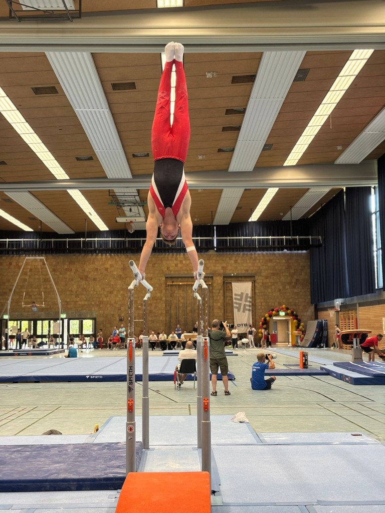 Turner beim Handstand auf den Parallelbarren in einer Turnhalle während eines Wettkampfs