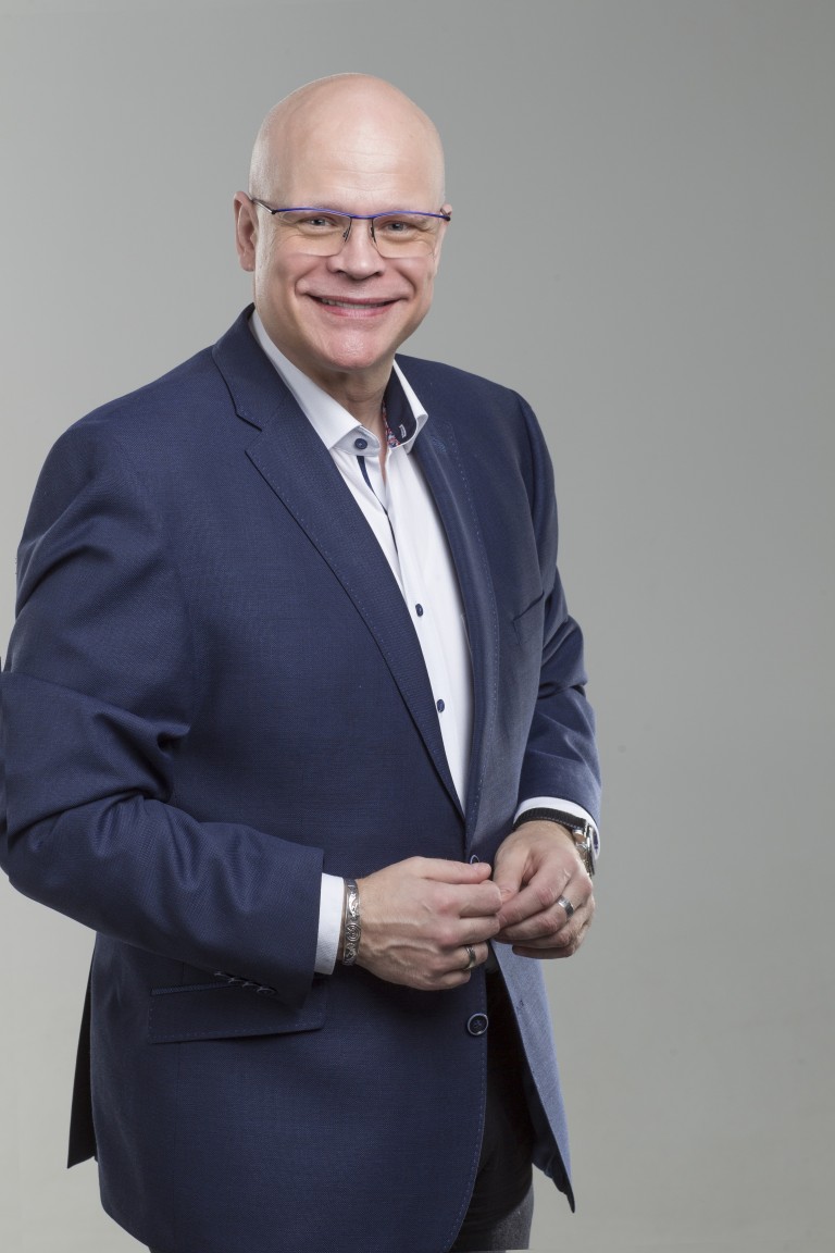 Dr. Thomas Ellwanger Lächelnder Mann in blauem Anzug mit Brille vor grauem Hintergrund