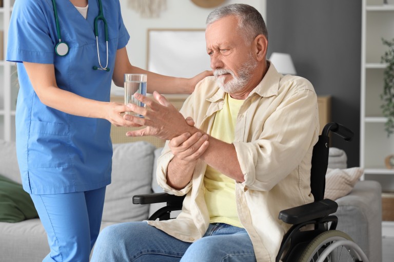 Pflegekraft hilft Senior im Rollstuhl mit einem Glas Wasser Pflegekraft reicht einem Senior im Rollstuhl ein Glas Wasser