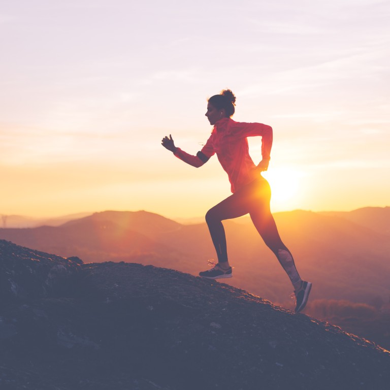 Frau beim Joggen auf einem Berg im Sonnenaufgang Frau joggt im Sonnenaufgang auf einem Berg
