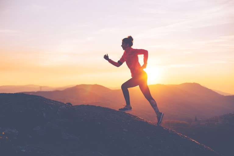 Frau beim Joggen auf einem Berg im Sonnenaufgang Frau joggt im Sonnenaufgang auf einem Berg