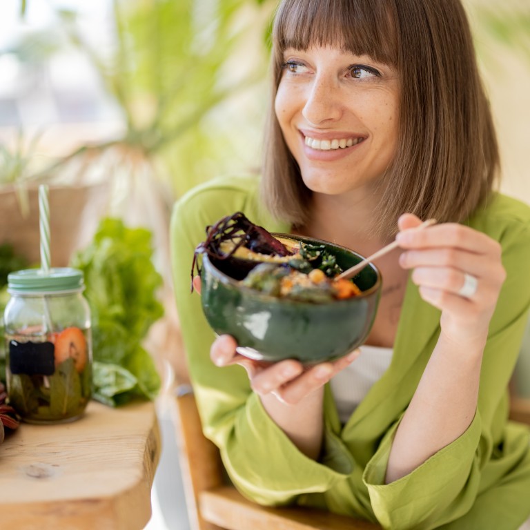 Frau isst veganen Salat und trinkt Detox-Wasser im Café Frau genießt gesunden veganen Salat und Detox-Getränk in modernem Café