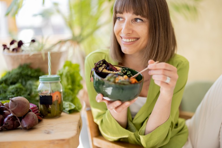Frau isst veganen Salat und trinkt Detox-Wasser im Café Frau genießt gesunden veganen Salat und Detox-Getränk in modernem Café