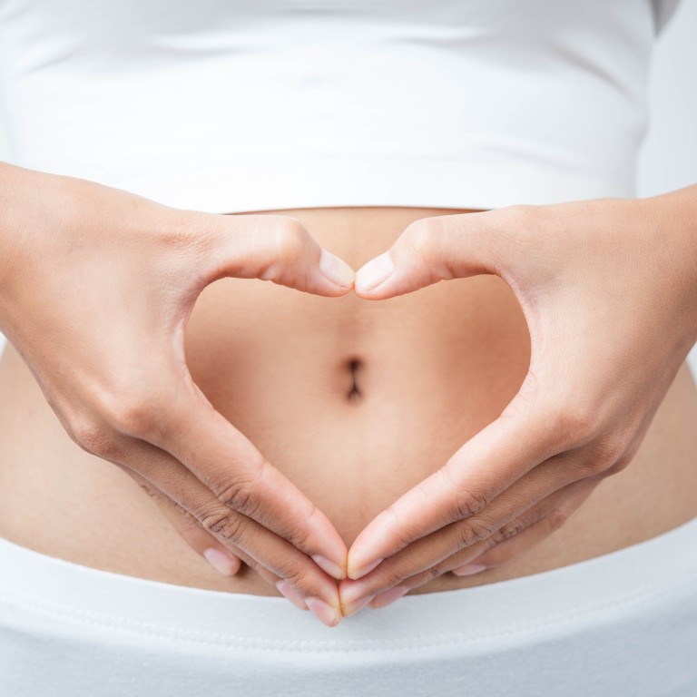 Frau mit Händen in Herzform vor dem Bauch – Symbol für Gesundheit und Wohlbefinden Frau hält ihre Hände in Herzform vor den Bauch, Symbol für Gesundheit und Wohlbefinden