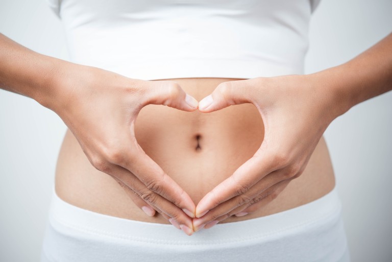 Frau mit Händen in Herzform vor dem Bauch – Symbol für Gesundheit und Wohlbefinden Frau hält ihre Hände in Herzform vor den Bauch, Symbol für Gesundheit und Wohlbefinden
