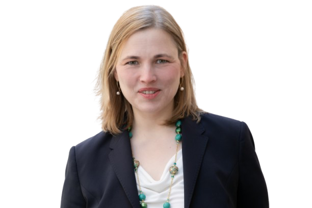 Frau mit blondem Haar, dunklem Blazer und grünem Schmuck vor schwarzem Hintergrund