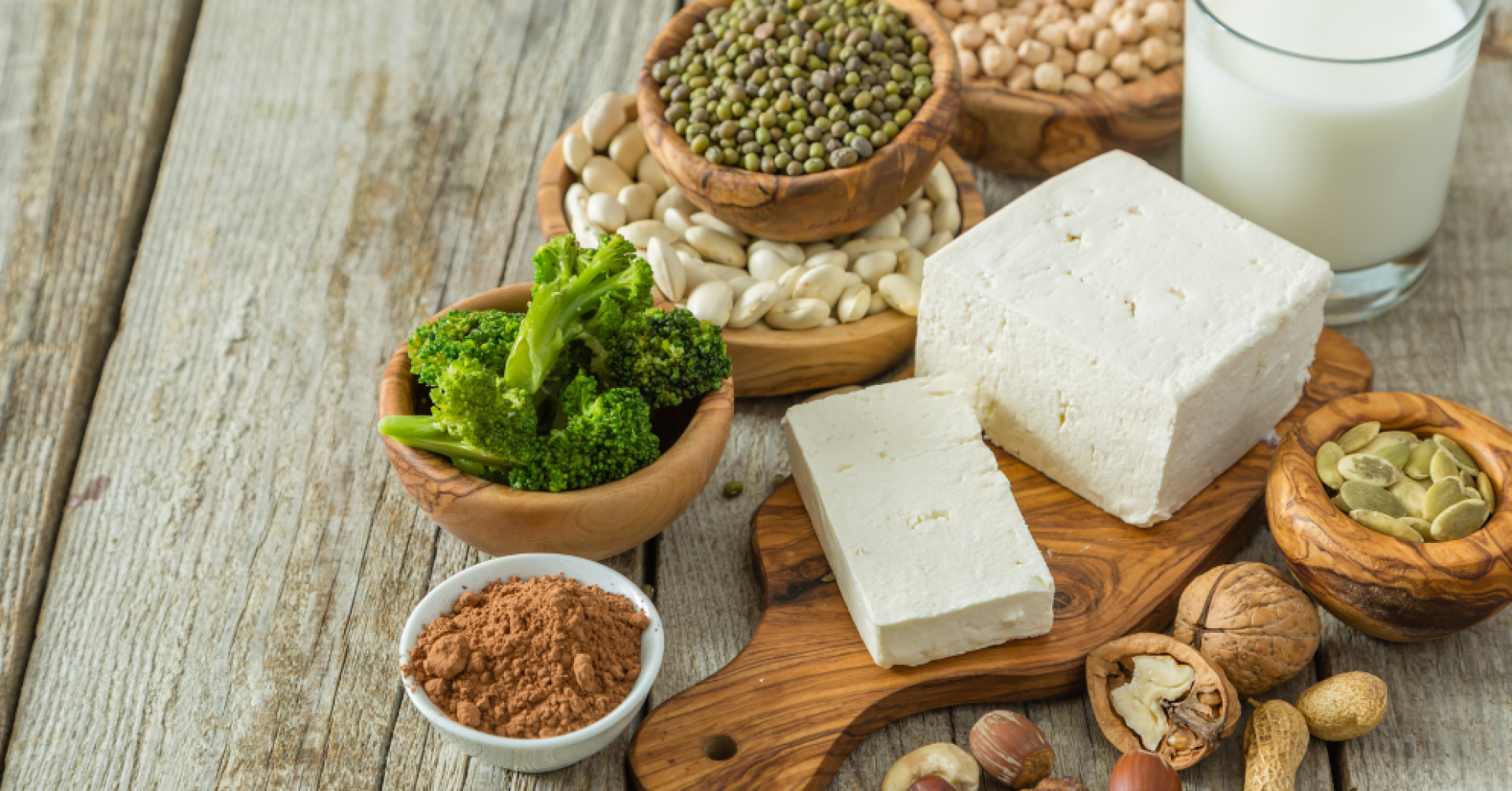 Verschiedene pflanzliche Proteinquellen wie Tofu, Nüsse und Hülsenfrüchte auf einem Holztisch