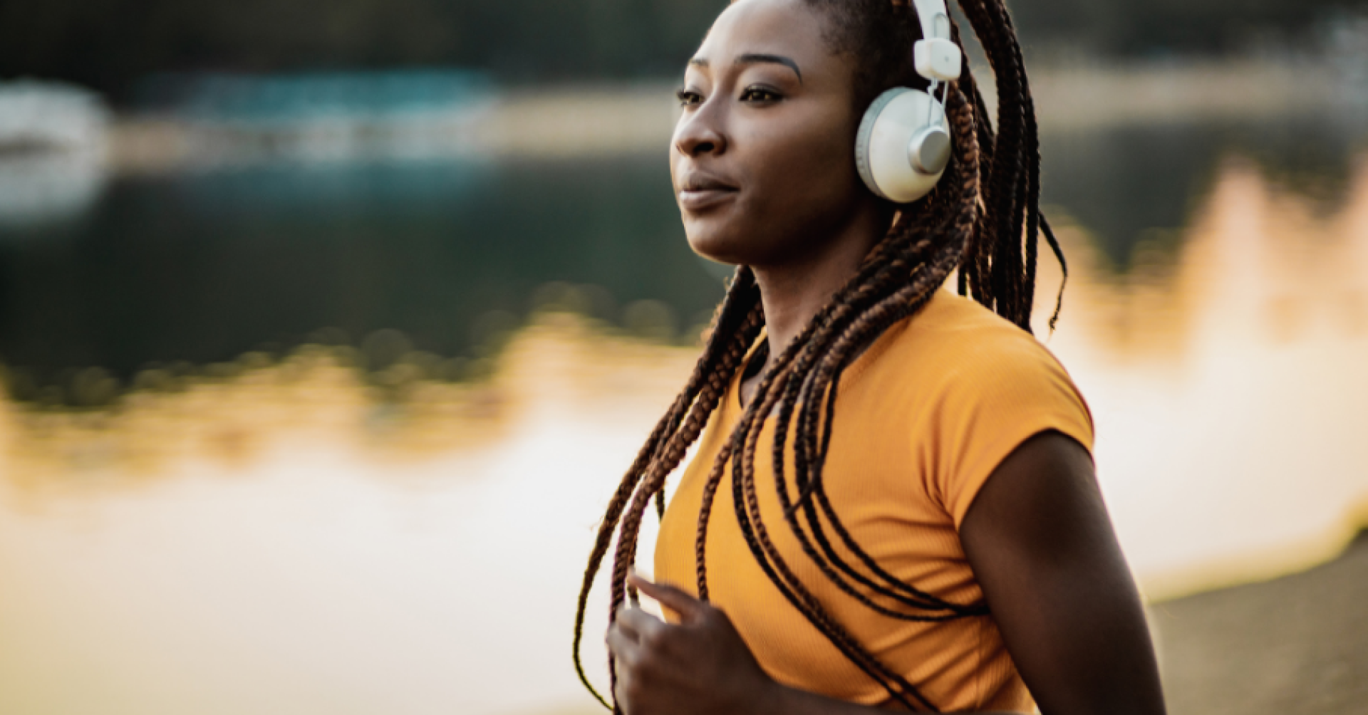Frau mit Kopfhörern joggt am Seeufer im Sonnenuntergang
