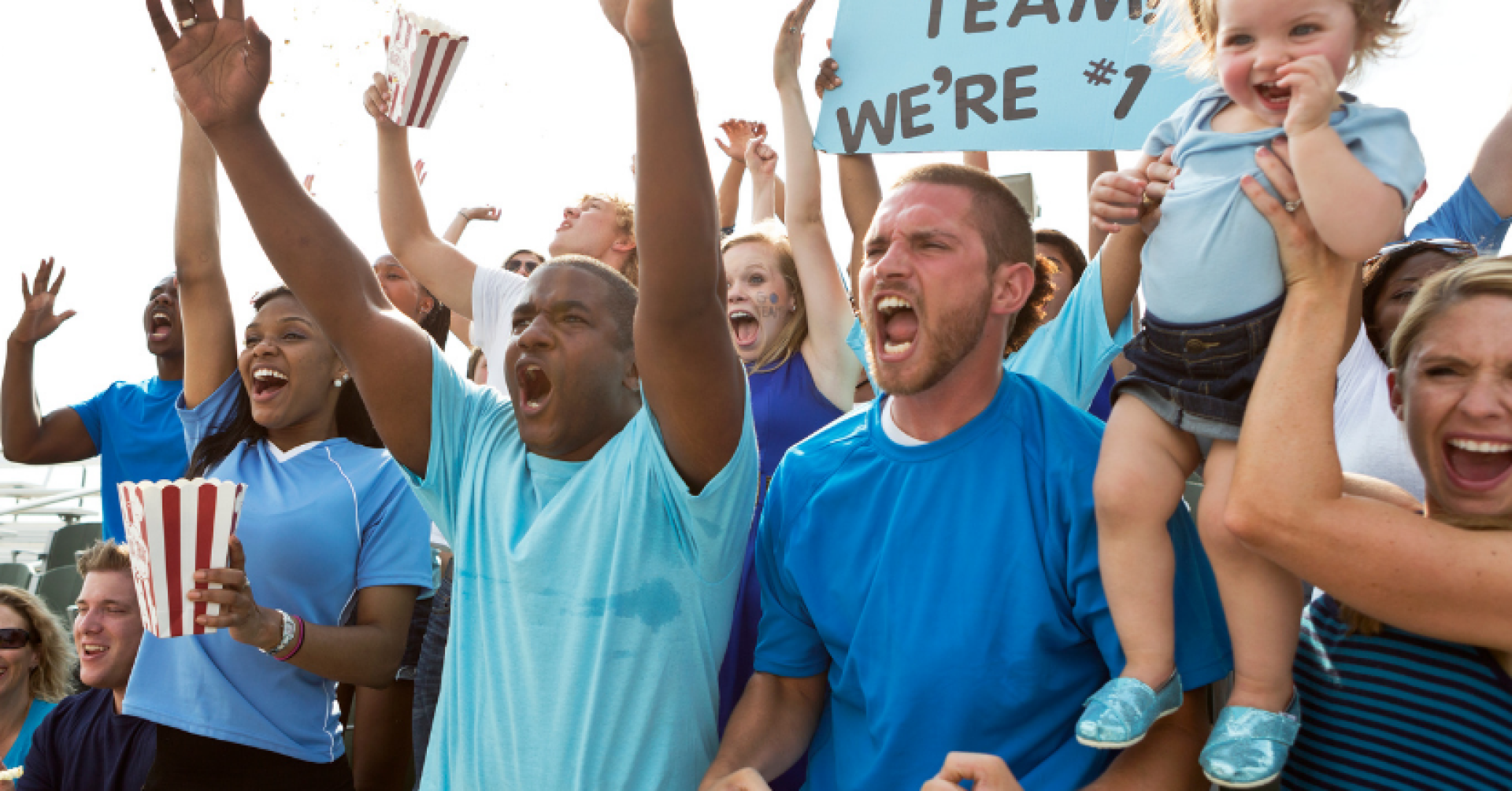 Jubelnde Fans bei einem Sportevent mit einem Schild 'Go Team, We're #1'