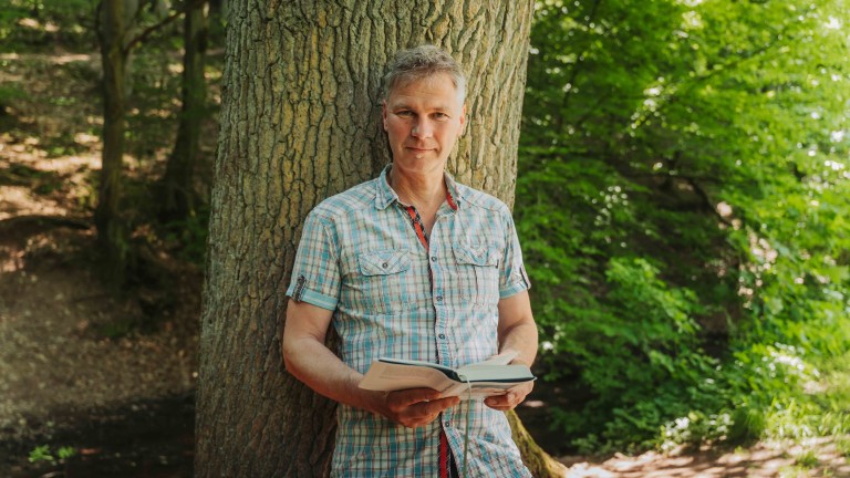 alea alternativ s 14 – Person liest Buch an Baum im Wald Person lehnt an Baum und liest ein Buch im Grünen – alea alternativ s 14