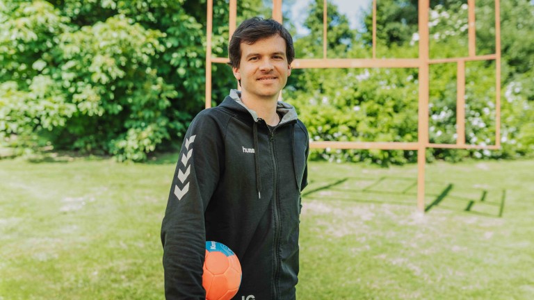Person mit schwarzer Hummel-Jacke und Handball, draußen auf einem Sportplatz – alea alternativ s 36