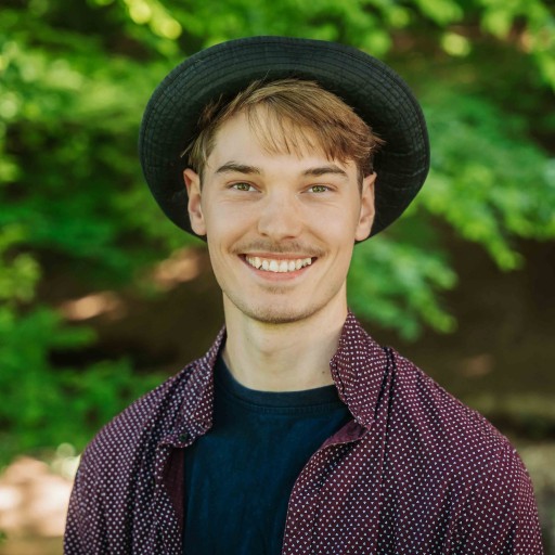 Alea Portrait S 21 – junger Mann mit Hut im Freien Alea Portrait eines jungen Mannes mit Hut und gemusterter Hemdjacke vor grünem Hintergrund