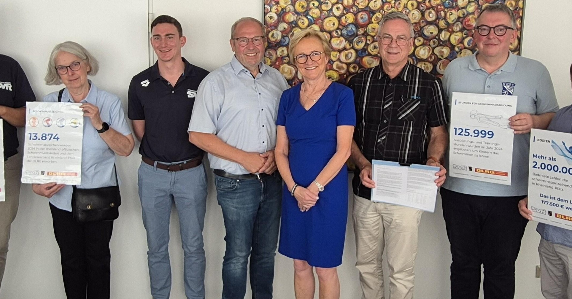 Gruppenbild mit Spendencheck-Präsentation Gruppe von Menschen bei der Präsentation eines Spendenchecks vor einem kunstvollen Hintergrund