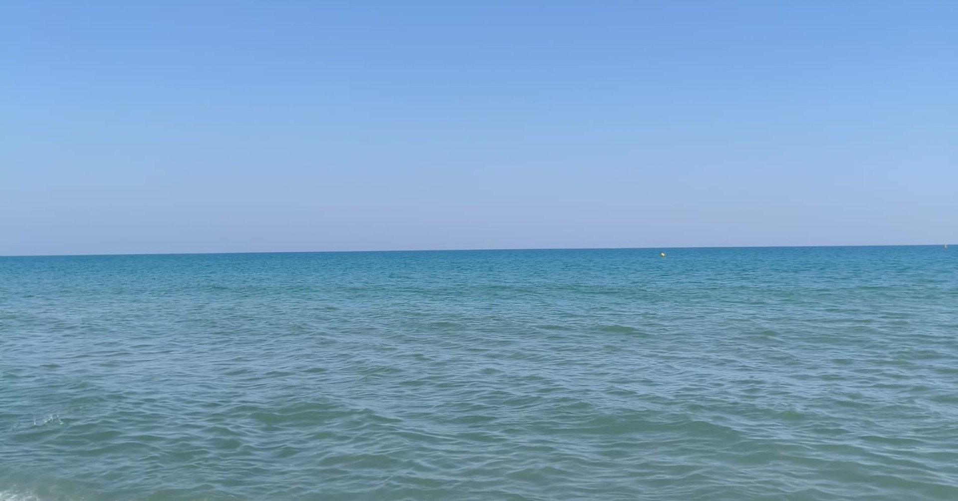Klares Meer mit sanften Wellen und blauem Himmel am Strand