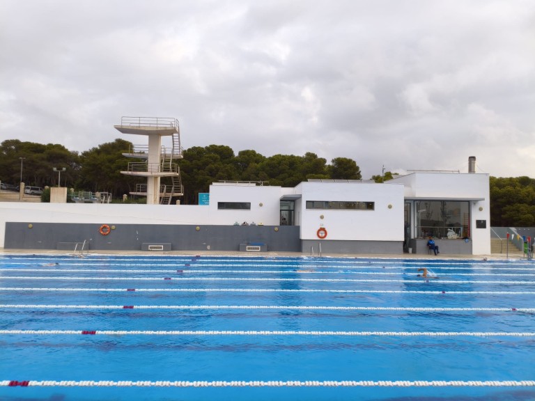 Außenansicht eines modernen Schwimmbads mit Sprungturm und mehreren Schwimmbahnen an einem bewölkten Tag