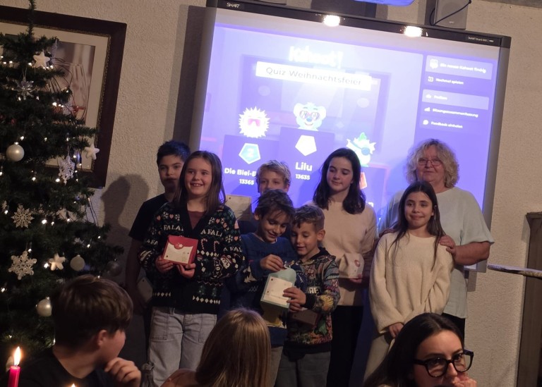 Kinder bei einer Weihnachtsfeier mit Kahoot Quiz und Geschenken vor einer Leinwand