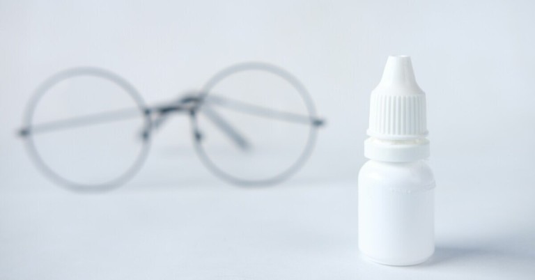 Augentropfen und Brille – Symbolbild für Augengesundheit Augentropfen-Flasche mit unscharfer Brille im Hintergrund