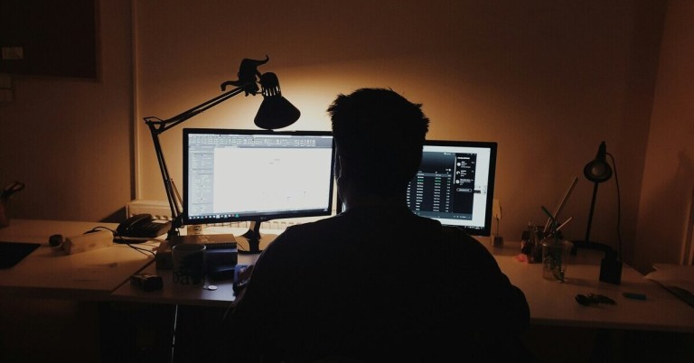 Mann am Bildschirm im Dunkeln – Arbeiten am Computer bei Nacht Mann sitzt im Dunkeln vor Bildschirm und arbeitet am Computer