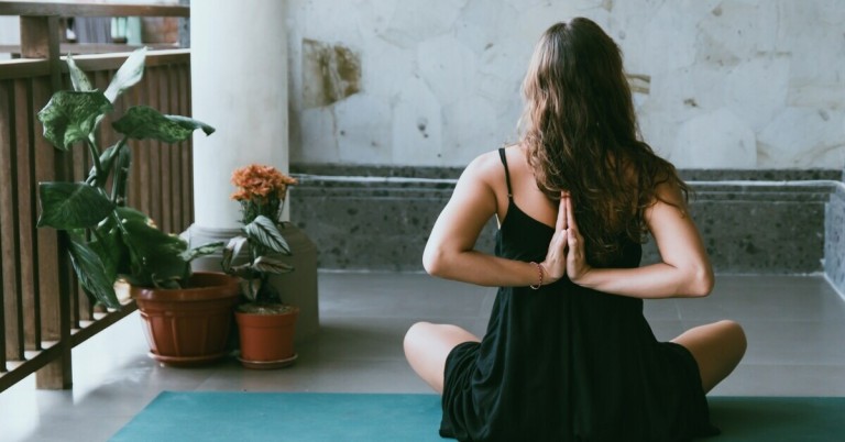 Übung zum Zusammenführen der Schulterblätter – Yoga-Position für eine bessere Schulterhaltung Übung zum Zusammenführen der Schulterblätter: Frau sitzt auf Yogamatte und hält die Hände hinter dem Rücken zusammen