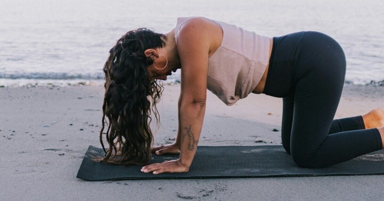 Kuh Yogahaltung (Bitilasana) – Yoga am Strand Frau in der Kuh Yogahaltung (Bitilasana) am Strand auf Yogamatte