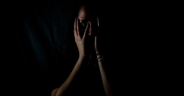Gesicht im Dunkeln Gesicht im Dunkeln, teilweise verdeckt von Händen, Symbol für Stress