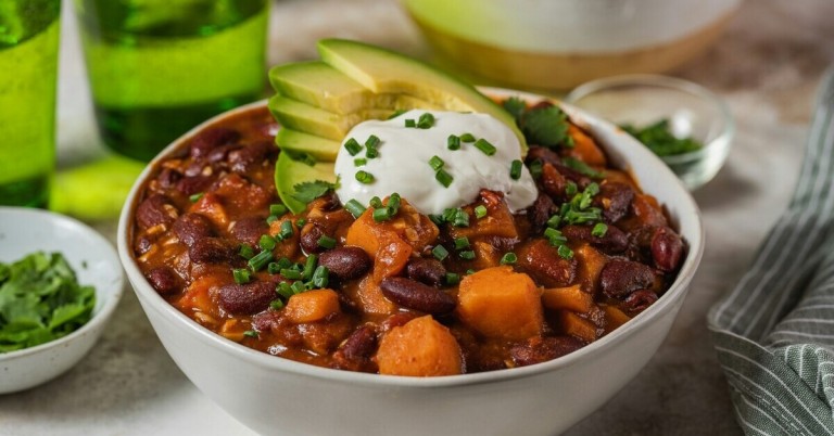 Herzhaftes Gericht mit Süßkartoffeln und Bohnen, garniert mit Avocado, Sauerrahm und Schnittlauch