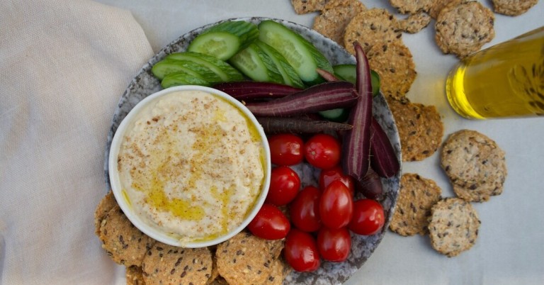 Hummus und Gemüsesnack mit Gurken, Karotten, Tomaten und Crackern auf einem Teller