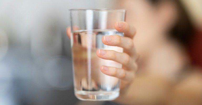 Hand hält ein Glas Wasser