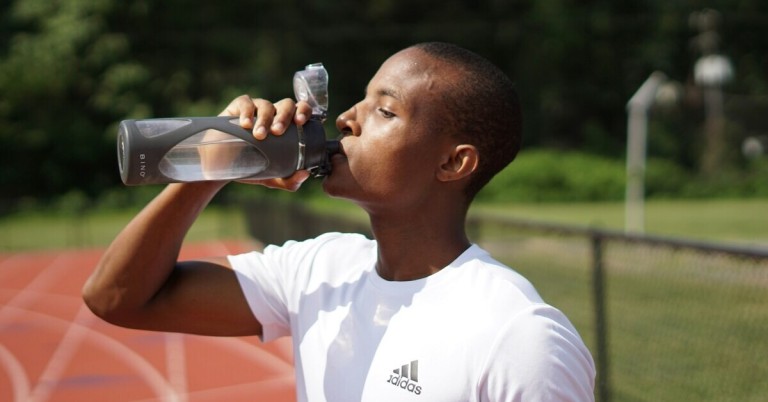 Sportler trinkt Wasser – Erfrischung beim Training auf der Laufbahn Sportler trinkt Wasser auf der Laufbahn im Freien