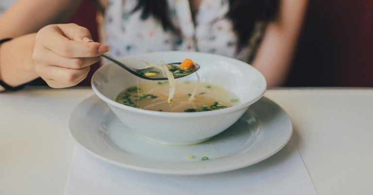 Frische Gemüsesuppe in einer weißen Schale, mit Möhren, Lauch und Nudeln, serviert auf einem Tisch