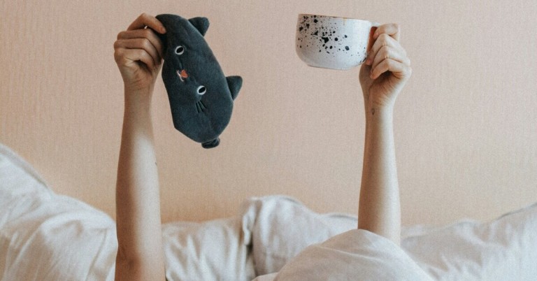 Kaffee vor dem Schlafen – Tasse und Schlafmaske im Bett Person hält eine Tasse Kaffee und eine Schlafmaske im Bett – Kaffee vor dem Schlafen