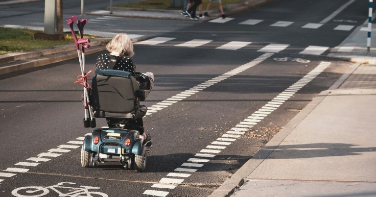 Seniorin fährt mit Elektromobil auf Straße und überquert Zebrastreifen