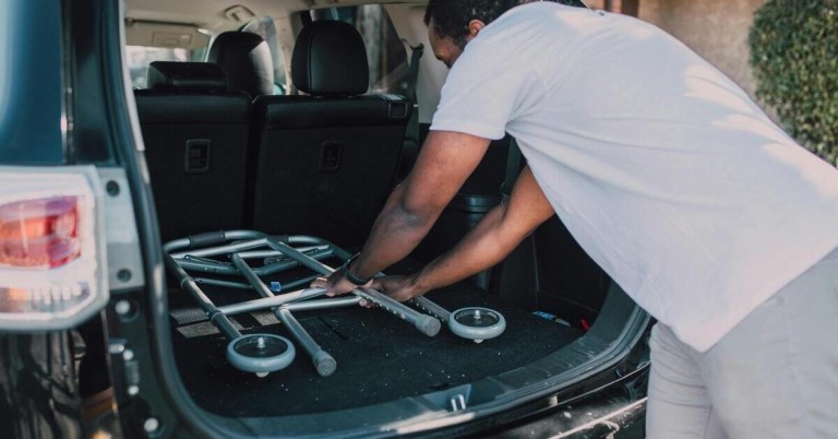 Mann zerlegt eine Gehhilfe im Kofferraum eines Autos