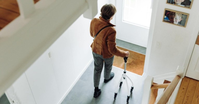 Ältere Frau mit Gehhilfe geht durch einen Flur