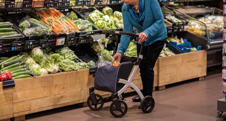 Seniorin mit Rollator beim Einkaufen im Supermarkt, legt Gemüse in die Rollator-Tasche.