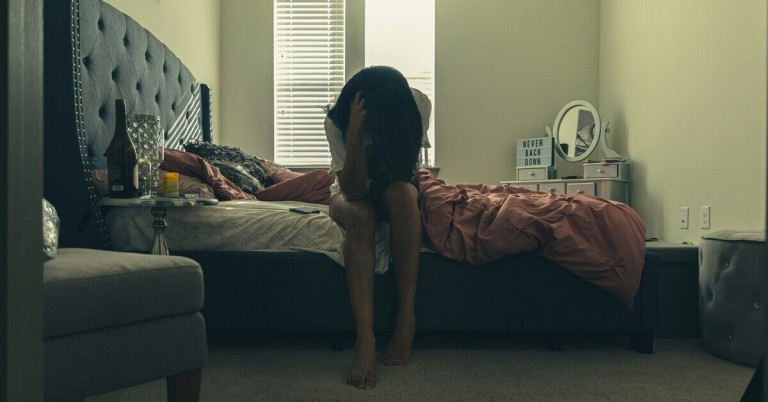 Frau mit Depression sitzt auf dem Bett im Schlafzimmer Frau sitzt auf dem Bett und wirkt depressiv in einem abgedunkelten Schlafzimmer