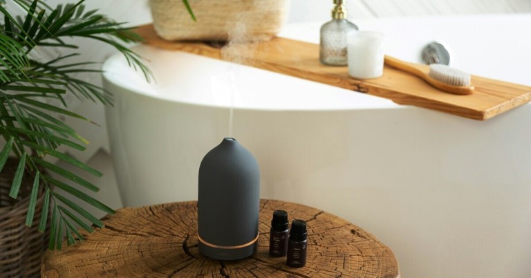 Moderner Luftbefeuchter mit ätherischen Ölen auf Holztisch vor Badewanne