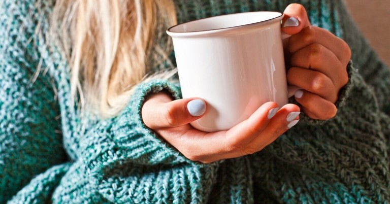 Frau hält weiße Tasse in der Hand, Nahaufnahme mit grünem Strickpullover