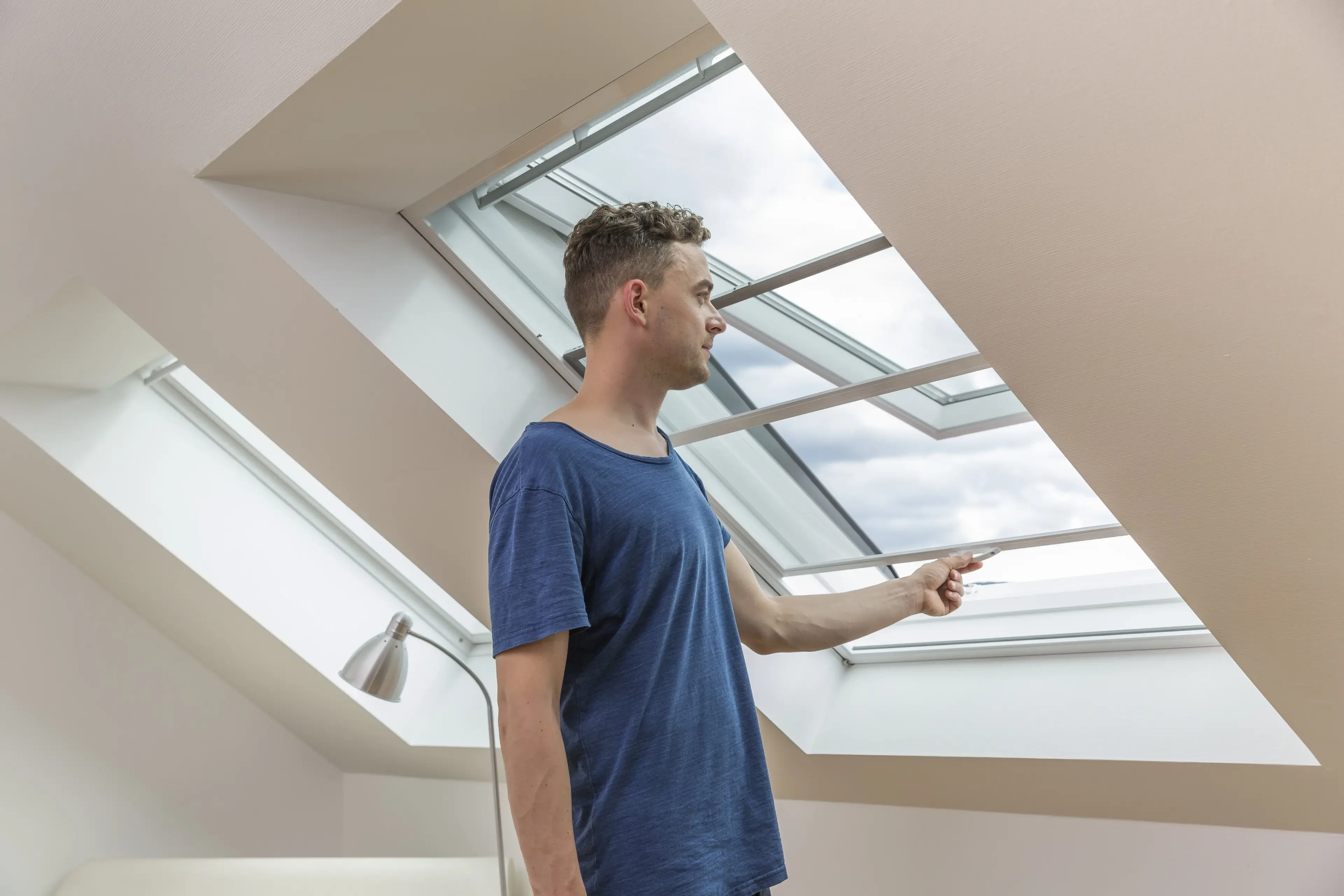 Mann im blauen T-Shirt öffnet ein Dachfenster in einer modernen Wohnung.