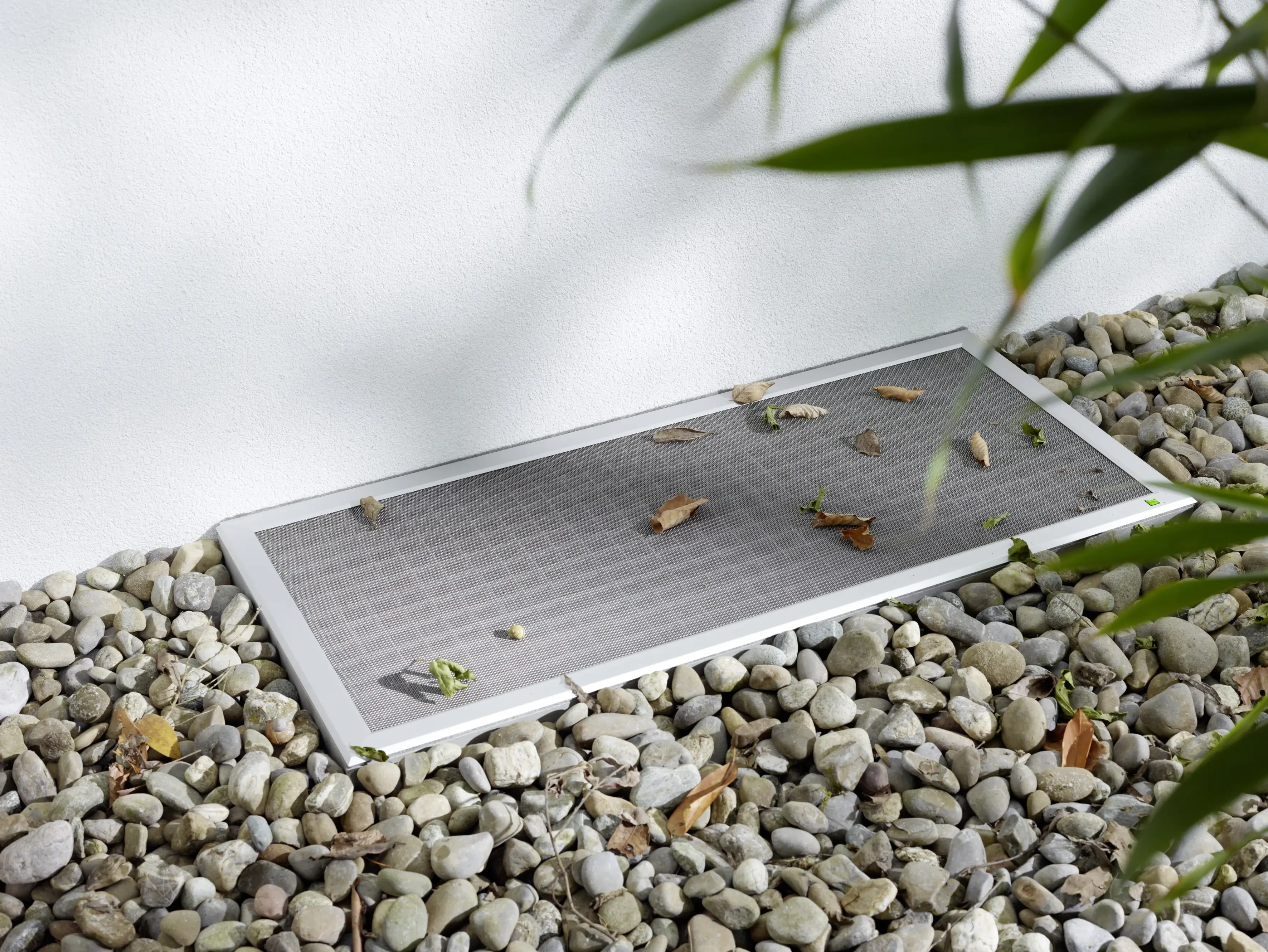 Lichtschachtabdeckung LISA mit fallenden Blättern und Kieselsteinen umrandet